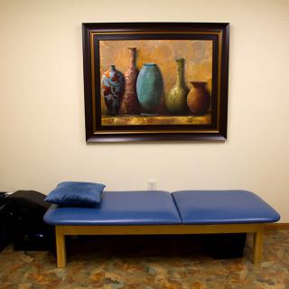 A therapy room with a treatment table and a painting on the wall.