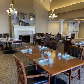 A cozy restaurant dining area with neatly arranged tables and chairs, featuring elegant chandeliers and a fireplace.