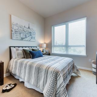 A cozy bedroom with a neatly made bed, artwork above the headboard, and natural light streaming through the window.