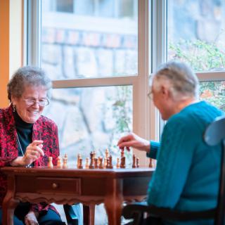 Two elderly people enjoying a game of chess indoors.