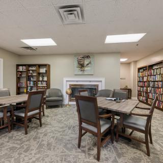 A cozy library room with tables, chairs, and shelves filled with books.