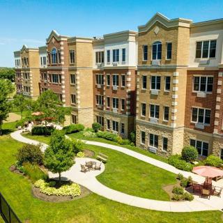 A landscaped area with a pathway and outdoor seating in front of a multi-story apartment building.