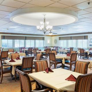 A well-lit dining room with neatly arranged tables and chairs, featuring a chandelier and large windows.