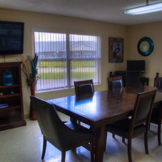 A well-lit meeting room featuring a wooden table, comfortable chairs, and a television.