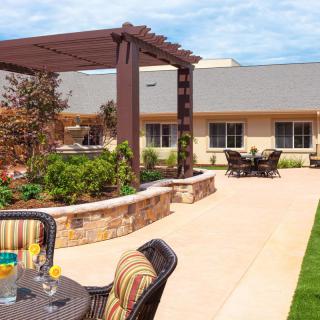 A sunny outdoor patio area featuring a pergola, comfortable seating, and landscaped garden.