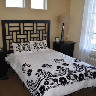 A stylishly decorated bedroom featuring a bed with black and white floral bedding, bedside tables, a lamp, and natural light from the window.