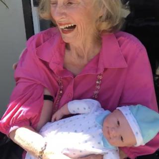 An elderly woman joyfully holds a baby while sitting outside.