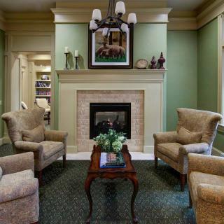 A cozy living room with a fireplace, surrounded by comfortable chairs and a small table.
