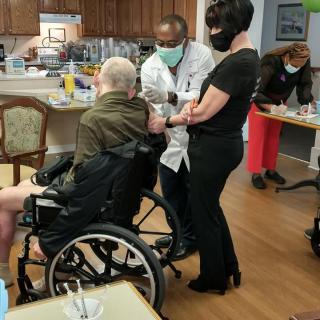 A healthcare professional administers a vaccine to an elderly person in a wheelchair at a nursing facility.