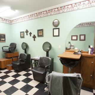 A cozy barber shop interior with chairs, mirrors, and hair dryers on a checkered floor.