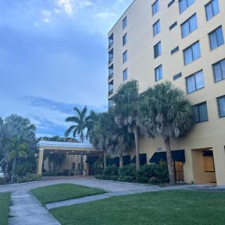 A view of a hotel surrounded by palm trees and a green lawn, under a cloudy sky.
