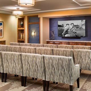 An interior view of a small theater room with rows of patterned chairs facing a large screen.