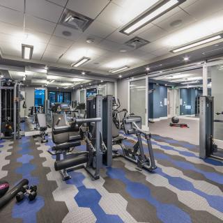 A modern gym with various exercise equipment and a geometric patterned floor.