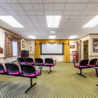 A conference room with rows of chairs facing a projector screen, decorated with curtains and framed posters.