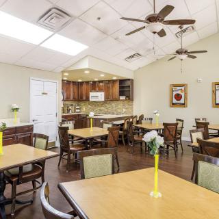 A cozy dining area with multiple tables and chairs, ceiling fans, and a view of a kitchen.