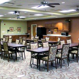 A spacious indoor dining area with multiple tables and chairs, featuring ceiling fans and a carpeted floor.