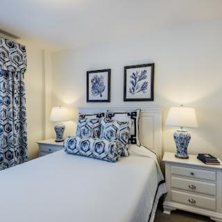 A cozy bedroom featuring a blue and white color scheme, adorned with decorative pillows, wall art, and stylish lamps.