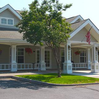A quaint house with a front porch and an American flag, surrounded by trees.