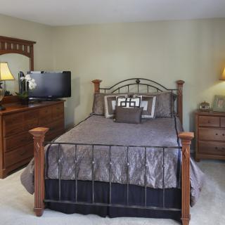 A cozy bedroom with a metal-framed bed, wooden dresser, and a TV.