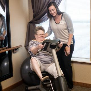 A senior woman receives assistance while using exercise equipment indoors.