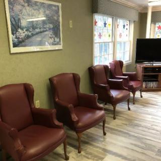 A cozy living room with red armchairs, a television, large windows, and a painting on the wall.