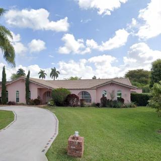 A suburban house with a well-maintained lawn and palm trees under a cloudy sky.