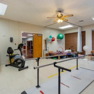 A therapy room equipped with exercise equipment including a stationary bike, parallel bars, and exercise balls.
