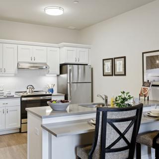 A modern kitchen with white cabinets and stainless steel appliances, featuring a small dining area with a countertop.