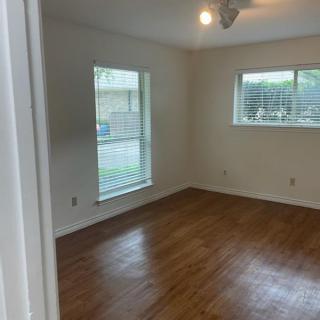 An empty room with hardwood floors and large windows letting in natural light.