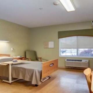 A hospital room with a bed and chair, featuring a window and medical equipment.