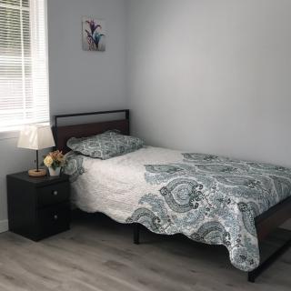 A minimalist bedroom featuring a single bed with patterned bedding, a nightstand with a lamp, and simple decor.