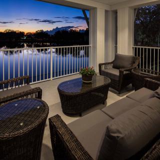 A cozy balcony overlooking a tranquil lake at sunset, furnished with comfortable rattan seating.