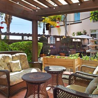 A cozy patio with comfortable seating under a pergola, surrounded by lush plants.