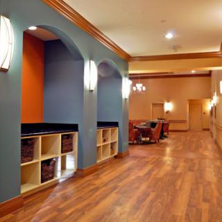 A modern hallway with vibrant orange and blue walls, featuring a wooden floor and seating area.