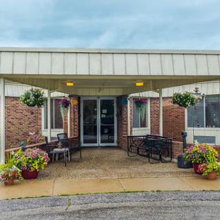 A welcoming entrance to a facility, featuring outdoor seating and colorful flower arrangements.
