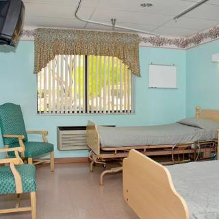 A hospital room with two beds, a window, and a television mounted on the wall.