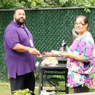 Two people preparing food on a barbecue grill in an outdoor garden setting.