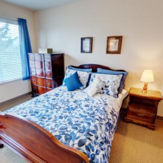 A cozy bedroom with a wooden bed, floral bedding, and a warm-lit lamp.