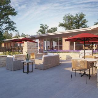 A modern outdoor patio with comfortable seating and sun umbrellas, set against a backdrop of trees.