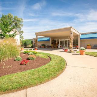 A beautifully landscaped entrance to a modern building, featuring a curved pathway and vibrant plants under a clear blue sky.