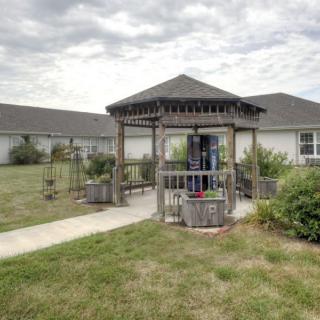 A wooden gazebo surrounded by a garden and pathway in an outdoor setting.