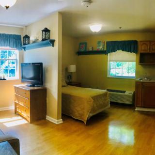 A cozy bedroom with a wooden floor, featuring a bed, dresser, TV, and large window.