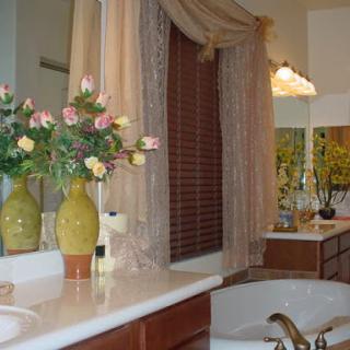 A beautifully decorated bathroom featuring floral arrangements, elegant curtains, and a spacious vanity area.