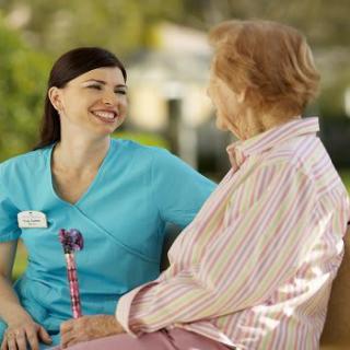 A nurse and an elderly woman smiling and conversing outdoors.