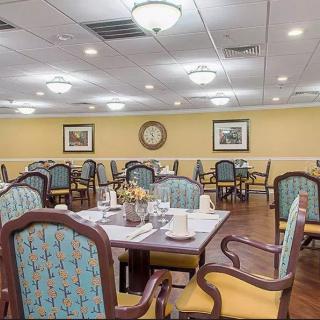 An elegantly furnished dining room with neatly arranged tables and chairs, softly lit by overhead lamps.