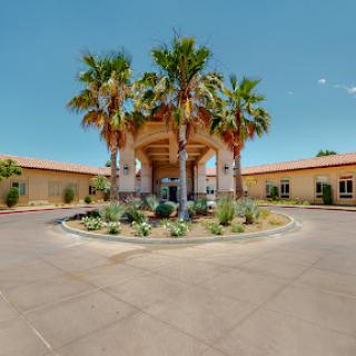 Entrance of a hotel featuring palm trees and a circular driveway under a clear blue sky.