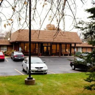 A small commercial building with a parking lot, surrounded by trees under an overcast sky.