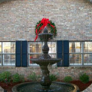 A decorative fountain in front of a brick wall adorned with a festive wreath and red bow.