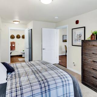 A modern bedroom with a plaid bedspread, wooden dresser, and open doorways leading to adjacent rooms.