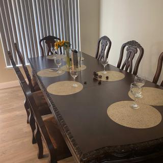 A dining table set with placemats and glassware, surrounded by wooden chairs.